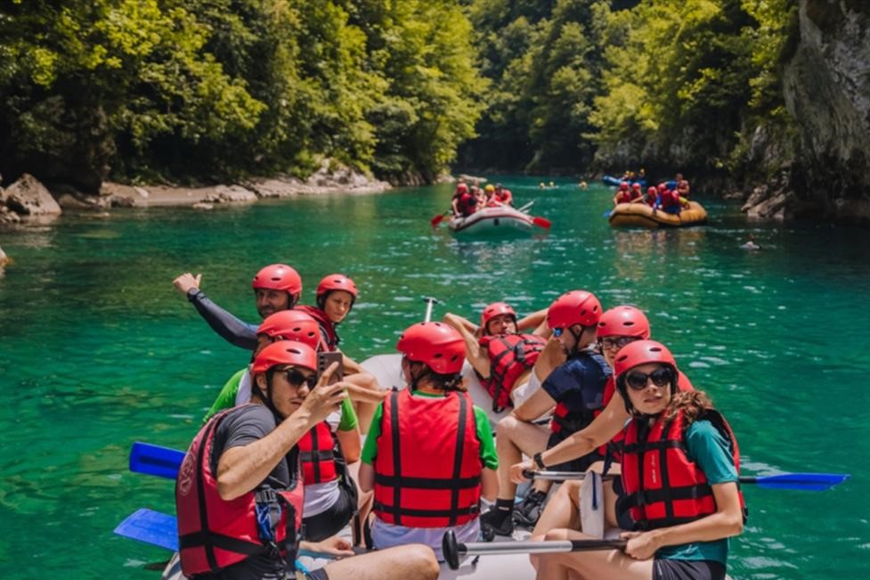Grupa ljudi u čamcu za rafting sa jos dva čamca ispred njih